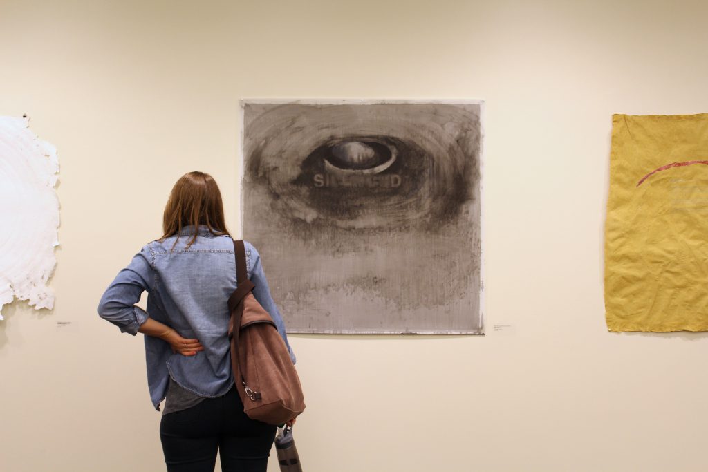 Photograph of a woman, seen from behind, standing in front of a drawing.