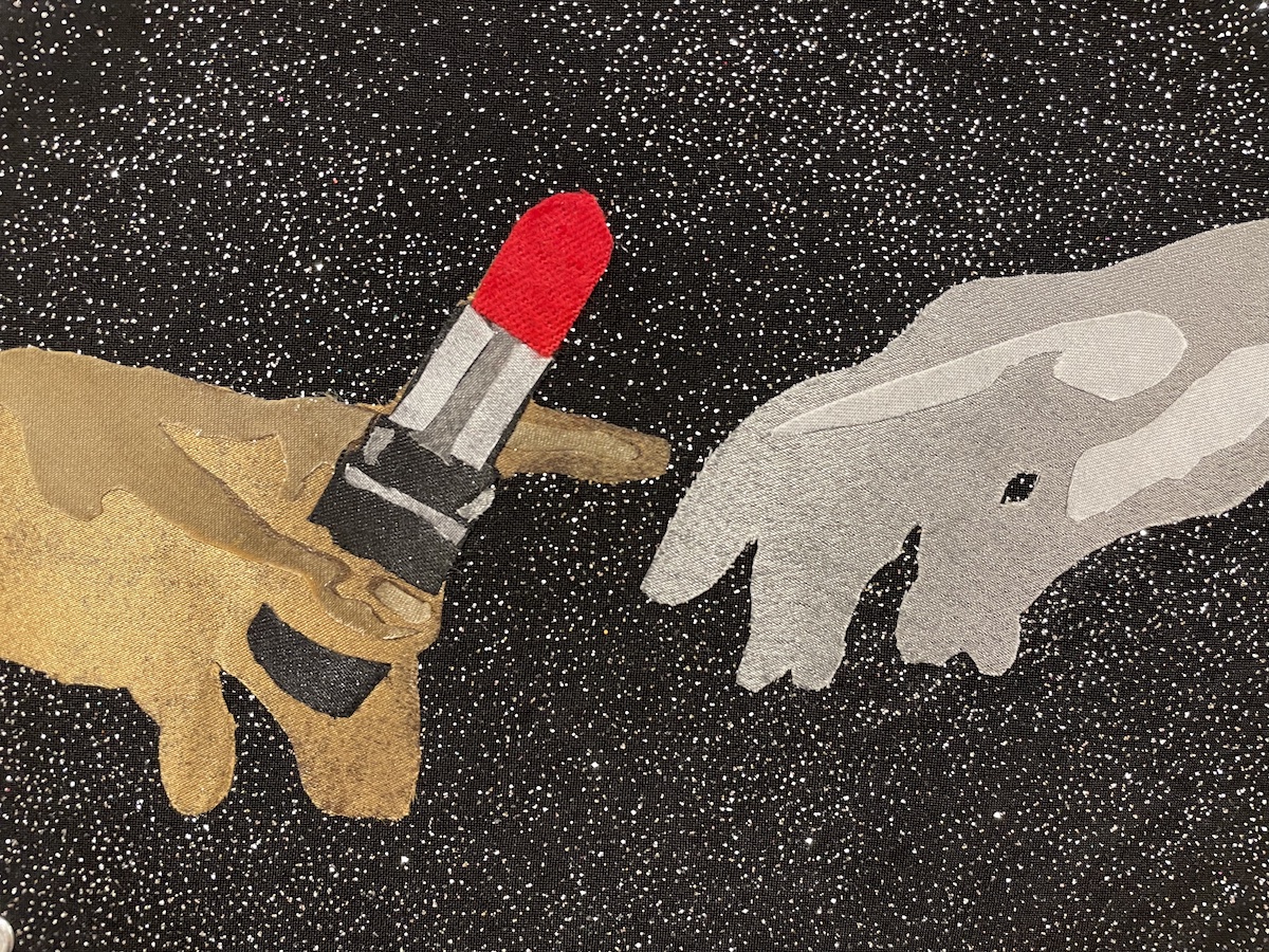 View of a textile artwork; one hand reachs for another. the hand on the left is golden and holds a tube of red lipstick, and reaches out for a pale silver hand. The black background is sewn through with sparkles.