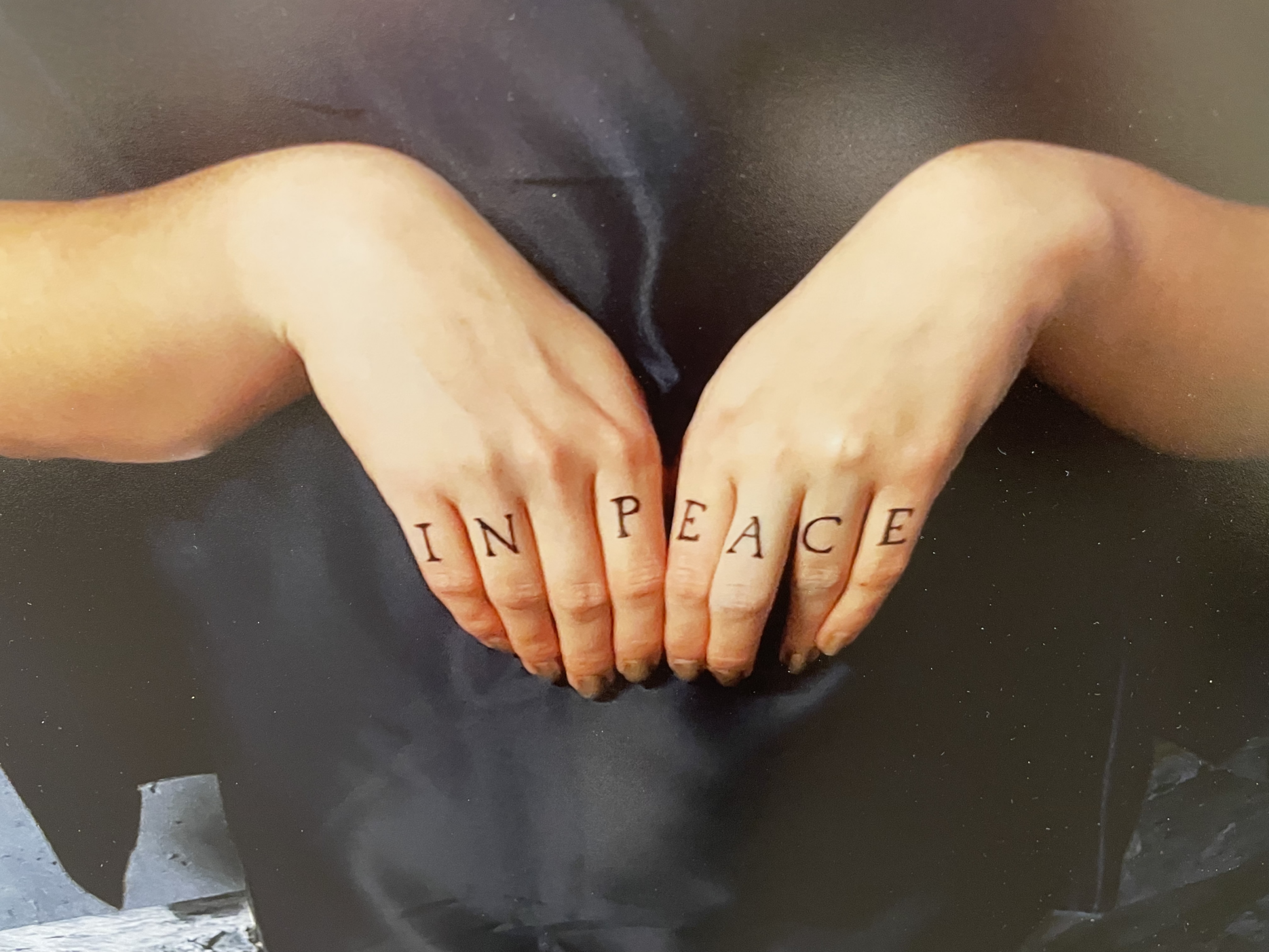 Detail from Jax Ohashi's photo "In Peace," showing a close-up of someone's hands with the letters IN PEACE written across the knuckles.