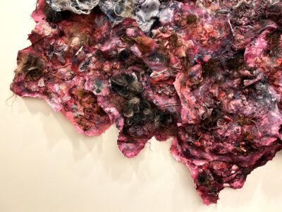 A section of a large paper sculpture imbued with hair and in bruised tones of red, purple, and green