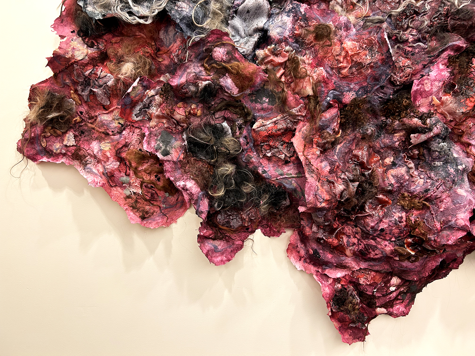 A section of a large paper sculpture imbued with hair and in bruised tones of red, purple, and green