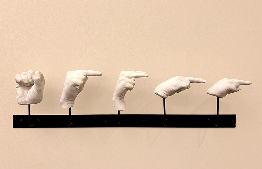 Sculpture of five hands cast in white plaster, spelling out the letters "SHHHH" in American Sign Language.